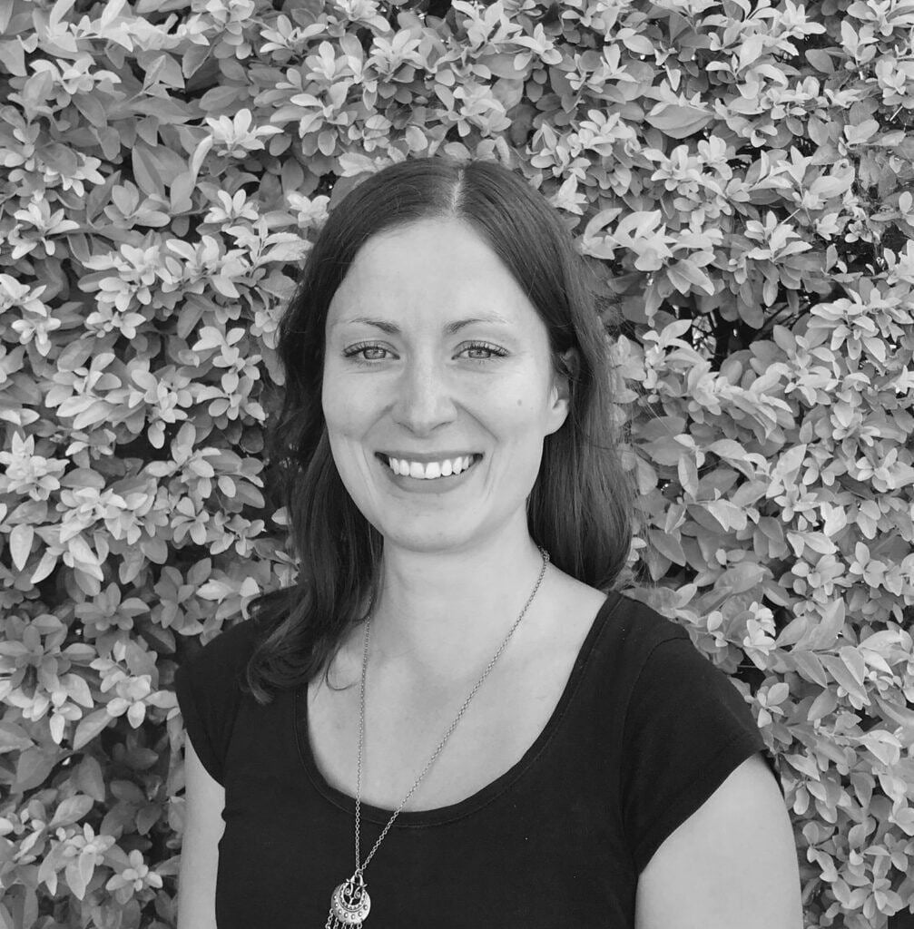 Psychologist Anu Johnson smiling in front of a leafy background, representing the Integrated Wellness Clinic's supportive mental health services for individuals of all ages.