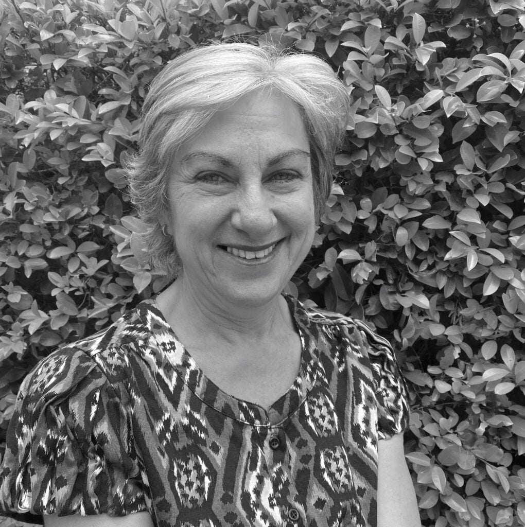 Irene Warren, smiling in front of green foliage, representing Integrated Wellness Clinic's supportive approach to mental health for children, adolescents, and adults.