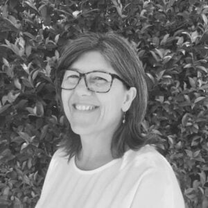 Lesley Baker, smiling woman with glasses, standing in front of greenery, representing the Integrated Wellness Clinic's focus on naturopathy and personalized health care.