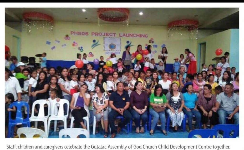 Celebration event at Gutalac Assembly of God Child Development Centre, featuring staff, children, and caregivers with colorful balloons and decorations, highlighting community support and engagement.