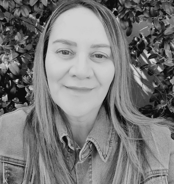 Deb Tawhai, Bundall psychologist and art therapist, smiling in front of greenery, promoting mental health support and therapy services at Integrated Wellness Clinic.