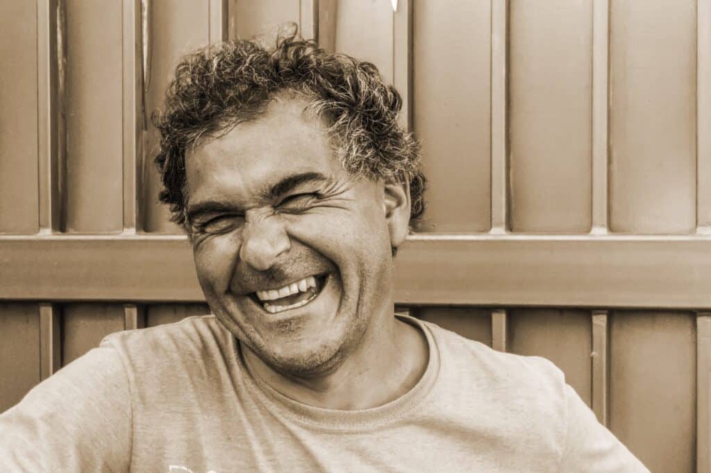 Smiling man with curly hair in casual attire, reflecting joy and well-being, representing positive men's health outcomes at Integrated Wellness Clinic.