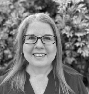 Melissa Callaghan, Naturopath specializing in complex conditions, digestion, thyroid issues, and mental health, smiling in front of greenery.