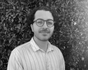 Kosta Sarinas, child psychologist at Integrated Wellness Clinic in Brisbane, standing against a leafy background, promoting children's psychological services.