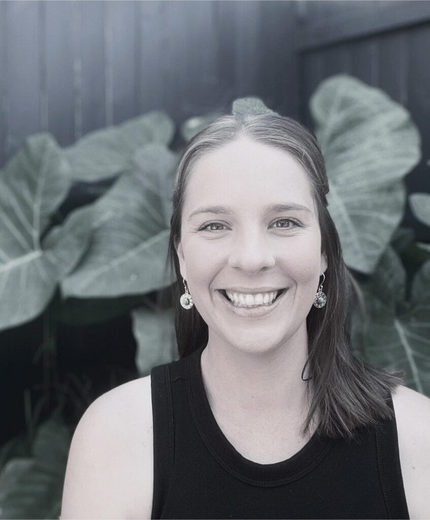 Megan Laws, Provisional Psychologist, smiling in a warm, inviting setting with lush green foliage, representing the supportive environment of the Integrated Wellness Clinic.