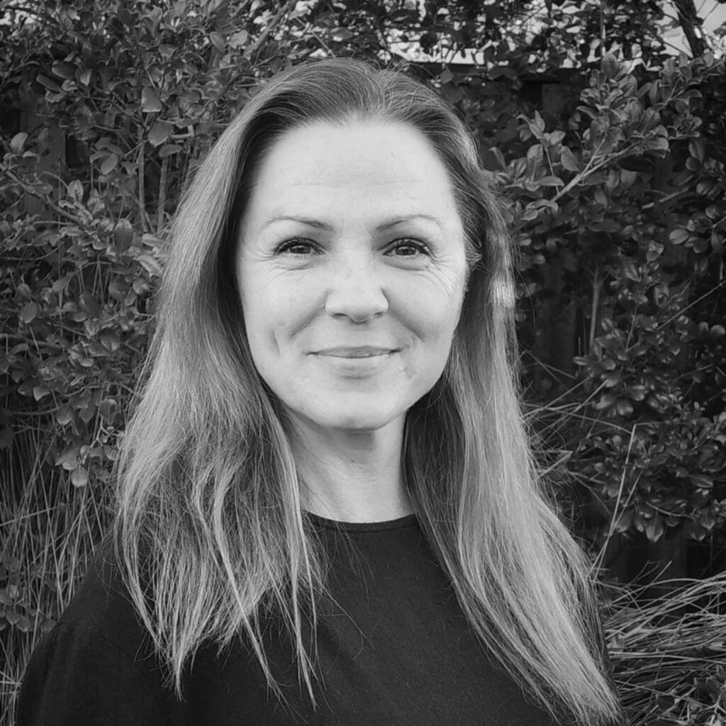 Smiling woman with long hair in a black shirt, standing outdoors among greenery, representing the Integrated Wellness Clinic's Sunshine Coast Naturopath team.