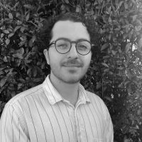 Psychologist Kosta Sarinas smiling in front of greenery, representing autism assessment services for ages 5-30 at Integrated Wellness Clinic in Brisbane.