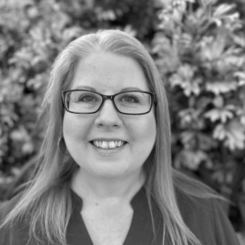 Melissa Callaghan, smiling with glasses, in front of greenery, representing expertise in digestion, mental health, and thyroid health at Integrated Wellness Clinic.