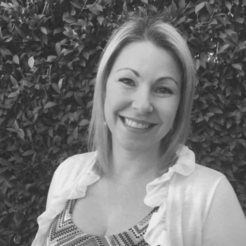 Smiling woman in a white cardigan against a green leafy background, representing the Integrated Wellness Clinic's focus on personalized naturopathy care for women's health and fertility.
