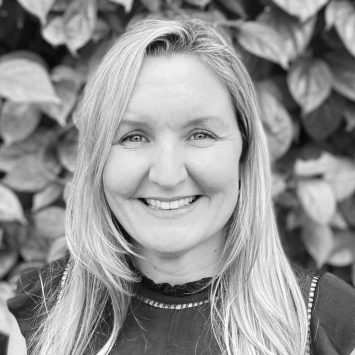 Psychologist smiling in front of leafy background, representing Integrated Wellness Clinic's supportive mental health services for adults and children.